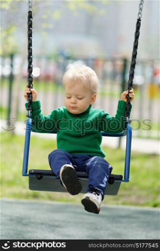 Portrait of toddler child outdoors. One year old baby boy wearing green sweater at playground swing
