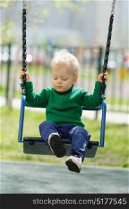 Portrait of toddler child outdoors. One year old baby boy wearing green sweater at playground swing