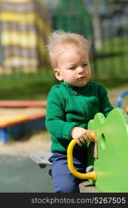 Portrait of toddler child outdoors. One year old baby boy wearing green sweater at playground seesaw