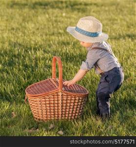 Portrait of toddler child outdoors. Rural scene with one year old baby boy wearing straw hat and picnic basket