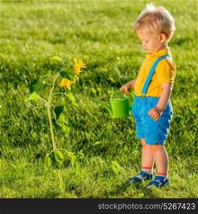 Portrait of toddler child outdoors. Rural scene with one year old baby boy using watering can for sunflower