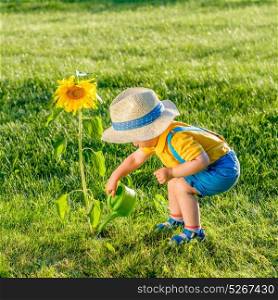 Portrait of toddler child outdoors. Rural scene with one year old baby boy wearing straw hat using watering can for sunflower