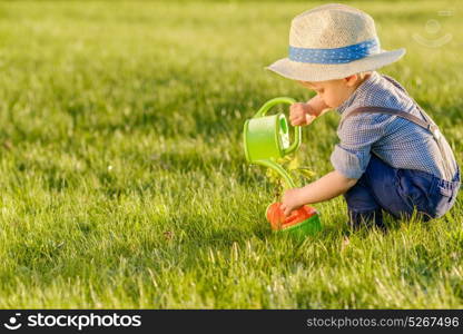 Portrait of toddler child outdoors. Rural scene with one year old baby boy wearing straw hat using watering can