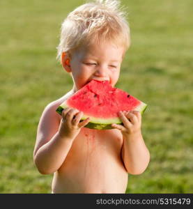 Portrait of toddler child outdoors. Rural scene with one year old baby boy eating watermelon slice in the garden. Dirty messy face of happy kid.