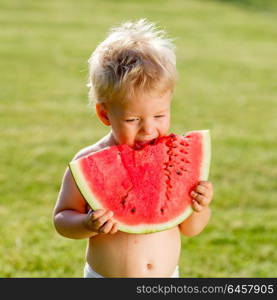 Portrait of toddler child outdoors. Rural scene with one year old baby boy eating watermelon slice in the garden. Dirty messy face of happy kid.