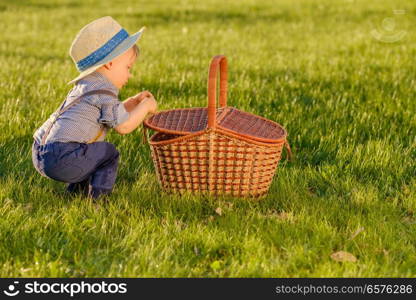 Portrait of toddler child outdoors. Rural scene with one year old baby boy wearing straw hat looking in picnic basket