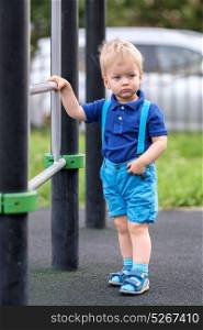 Portrait of toddler child outdoors wearing shorts and suspenders. One year old baby boy at playground