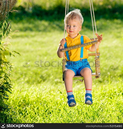 Portrait of toddler child swinging outdoors. Rural scene with one year old baby boy at swing. Healthy preschool children summer activity. Kid playing outside.