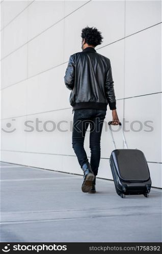 Portrait of tourist man carrying suitcase while walking outdoors on the street. Tourism concept.