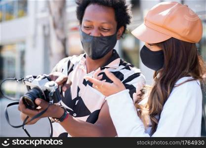 Portrait of tourist young couple wearing protective mask and using camera while taking photographs in the city. Tourism concept. New normal lifestyle concept.