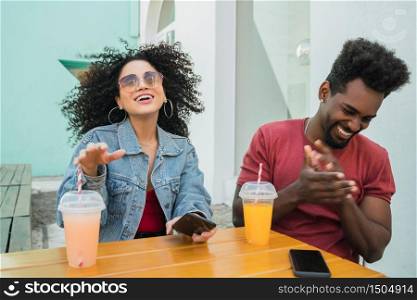 Portrait of two Afro friends having fun together and enjoying good time while drinking fresh fruit juice outdoors at cafeteria.