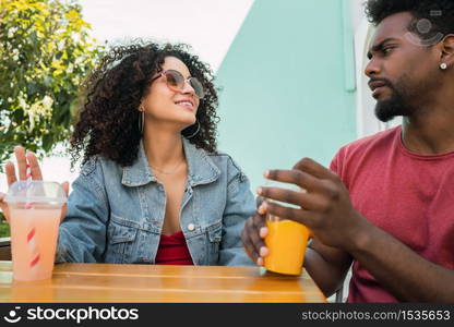 Portrait of two Afro friends having fun together and enjoying good time while drinking fresh fruit juice outdoors at cafeteria.