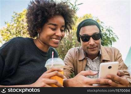 Portrait of two Afro friends using their mobile phone at coffee shop. Friendship and lifestyle concept.