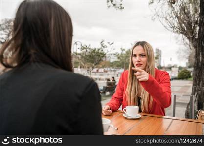 Portrait of two angry friends having a serious conversation and discussing while sitting at coffee shop. Friendship concept.