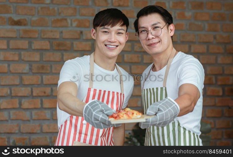 Portrait of two Asian handsome men cooking and holding a dish of pizza. Lifestyle and LGBT Concept.