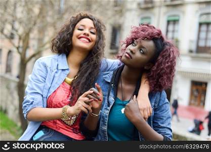 Portrait of two beautiful girls in urban backgrund, black and mixed women. Friends talking