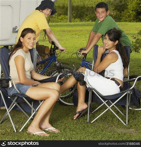 Portrait of two boys sitting on bicycles with two teenage girls sitting on armchairs and smiling