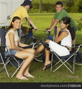 Portrait of two boys sitting on bicycles with two teenage girls sitting on armchairs and smiling