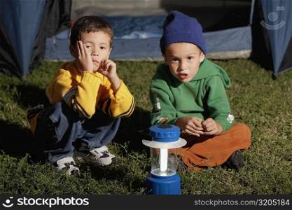 Portrait of two boys sitting together in front of a tent