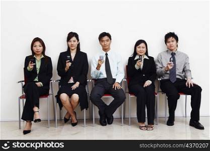 Portrait of two businessmen and three businesswomen sitting together and holding mobile phones