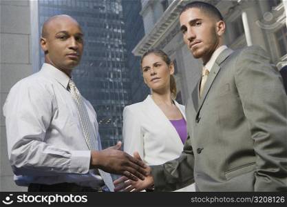 Portrait of two businessmen shaking hands with a businesswoman standing beside them