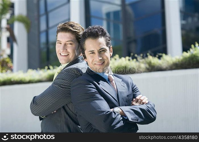 Portrait of two businessmen standing back to back and smiling