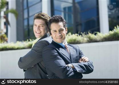 Portrait of two businessmen standing back to back and smiling