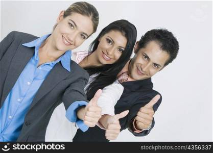 Portrait of two businesswomen and a businessman standing in a row and making a thumbs up sign