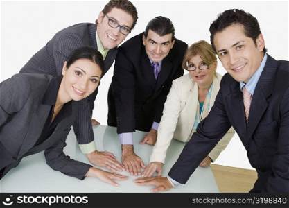 Portrait of two businesswomen and three businessmen placing their hands on the table