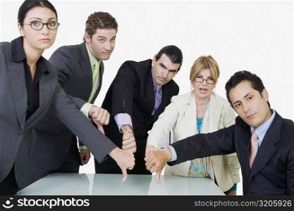 Portrait of two businesswomen and three businessmen showing thumbs down sign