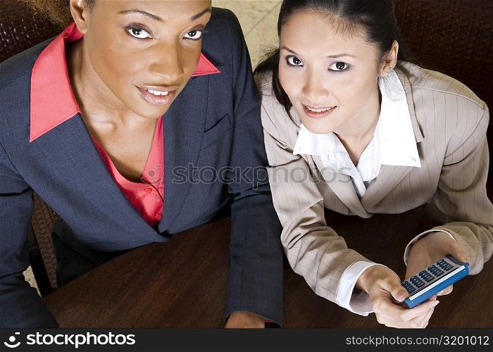 Portrait of two businesswomen smiling holding a calculator