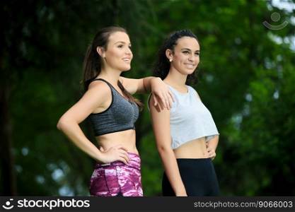 Portrait of two cheerful friends in sportswear smiling away against of green background in park of Cordoba,Spain.Bokeh