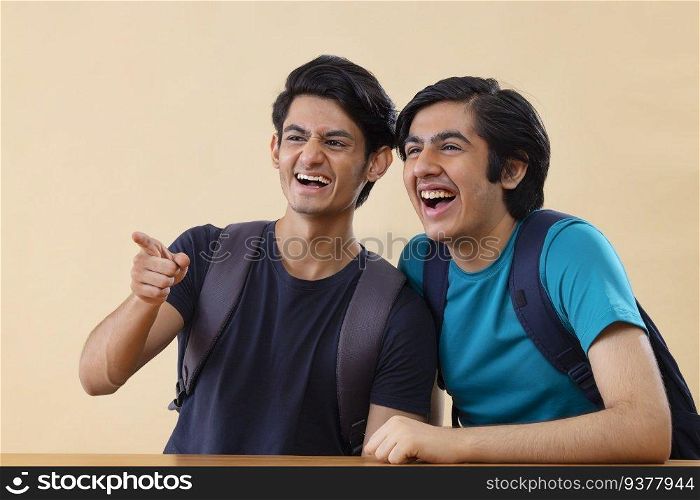 Portrait of two cheerful teenage boys pointing elsewhere against plain background