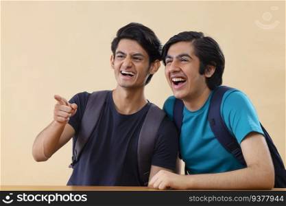 Portrait of two cheerful teenage boys pointing elsewhere against plain background