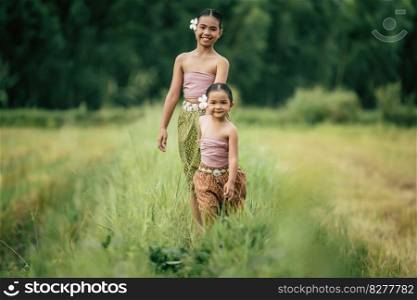 Portrait of two Cute girls in Thai traditional dress walking on rice field, They are smile with happiness and looking at camera, copy space