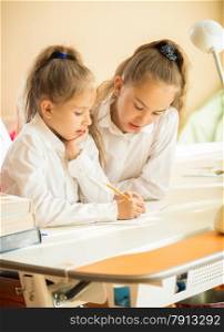 Portrait of two cute schoolgirls writing at textbook at desk