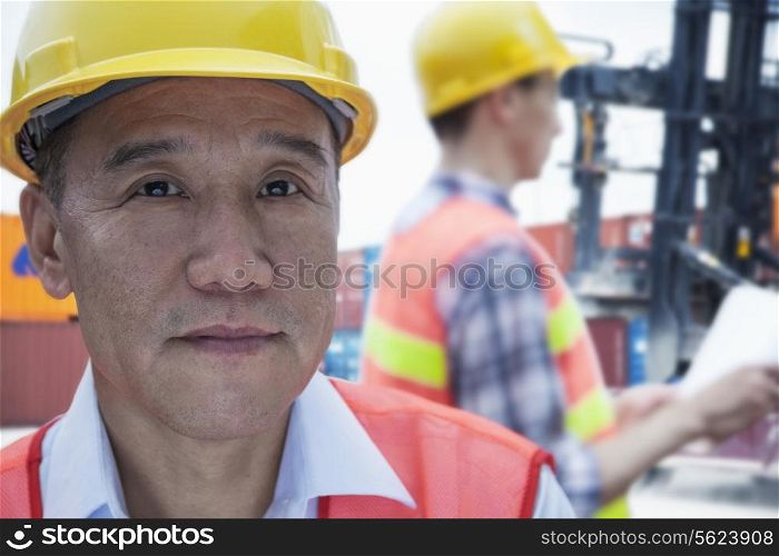 Portrait of two engineers in protective workwear working, looking at camera, outside in a shipping yard