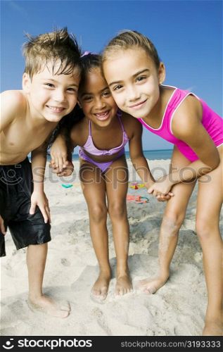 Portrait of two girls and a boy standing on the beach and smiling