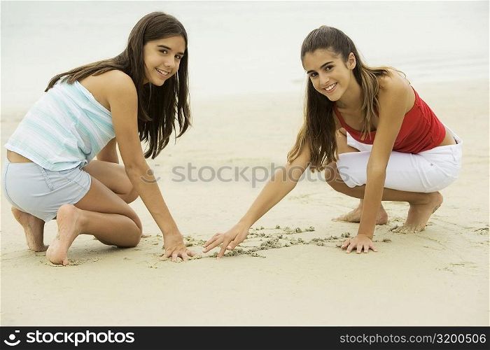 Portrait of two girls drawing in sand on the beach