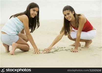 Portrait of two girls drawing in sand on the beach