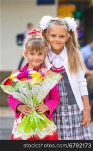 Portrait of two girls in school September 1 - the first-grader and her younger sister with a bouquet in hands