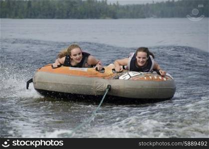Portrait of two girls lying on an inflatable raft floating in a lake, Lake Of The Woods, Ontario, Canada