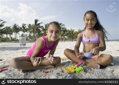 Portrait of two girls sitting on the beach and playing with sand