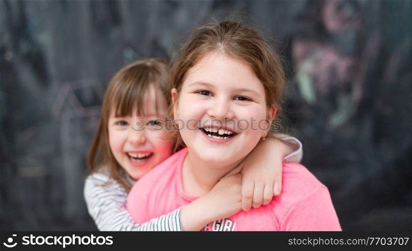 portrait of two happy cute little girls hugging each other while having fun in front of black chalkboard