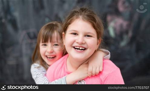 portrait of two happy cute little girls hugging each other while having fun in front of black chalkboard