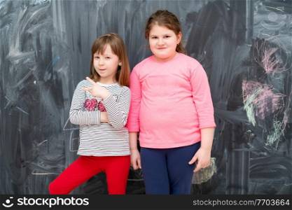 portrait of two happy cute little girls standing in front of black chalkboard