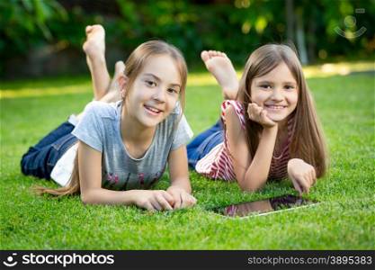 Portrait of two happy girls using digital tablet on grass at park