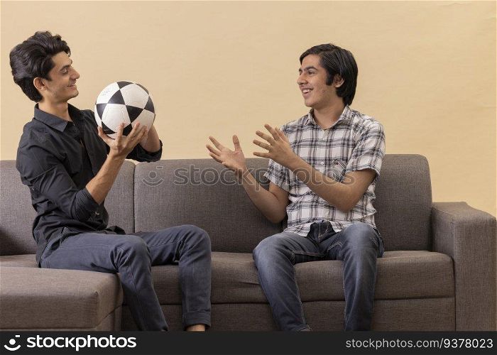 Portrait of two happy teenage boys playing football indoors 