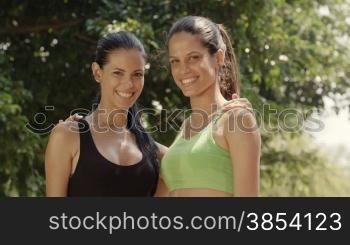 Portrait of two happy young women meeting and smiling after exercising in city park. Slow motion