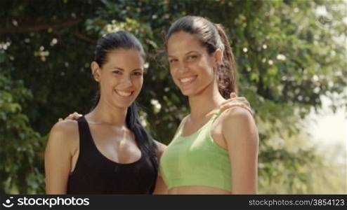 Portrait of two happy young women meeting and smiling after exercising in city park. Slow motion